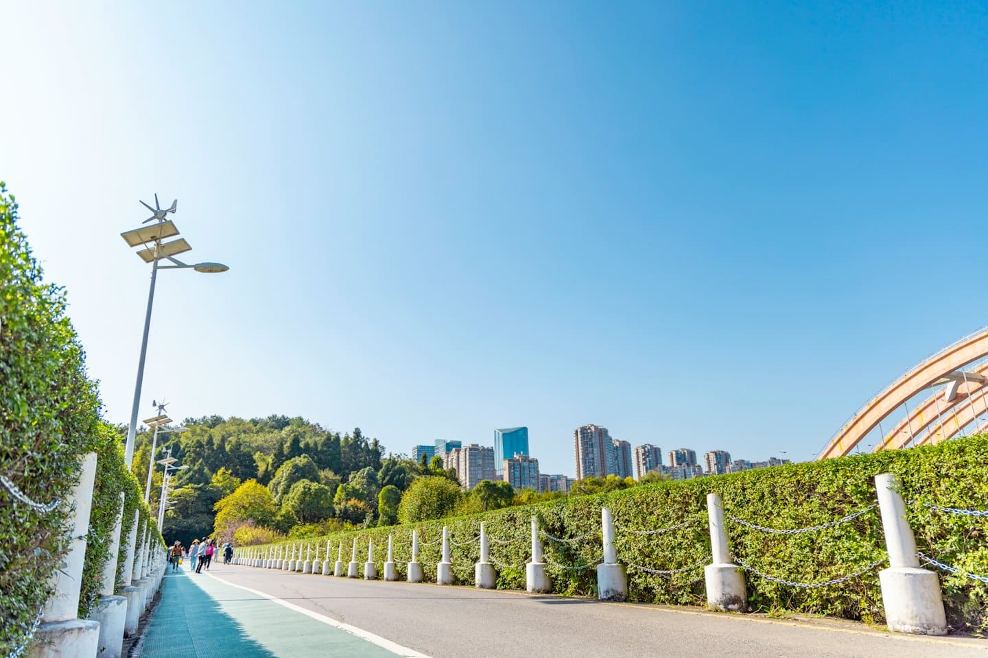 People walk along a paved path lined with sustainable streetlights.